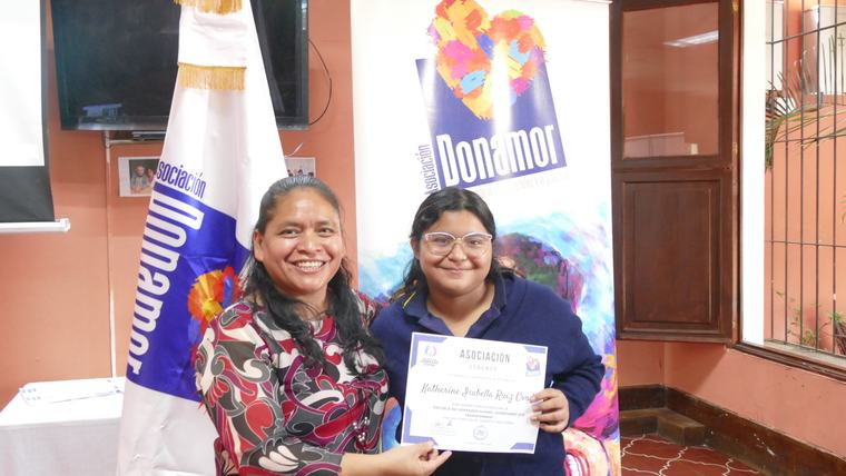 Participante recibiendo su diploma frente al banner de Donamor
